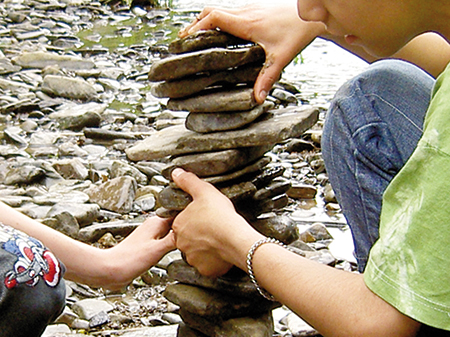 Kinder stapeln an einem kleinen Bach flache Steine übereinander.